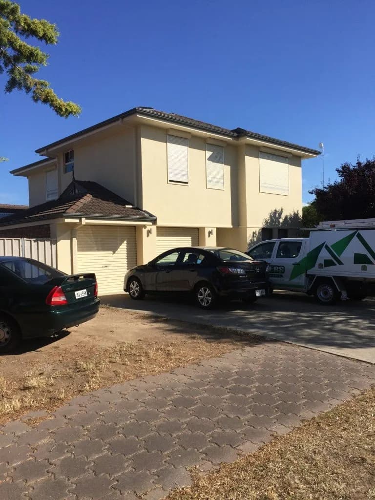 Two-storey home extension with a cream render facade, roller shutters and driveway